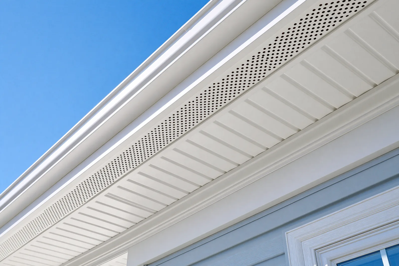 A perforated soffit vent strip runs along a white eave under blue sky